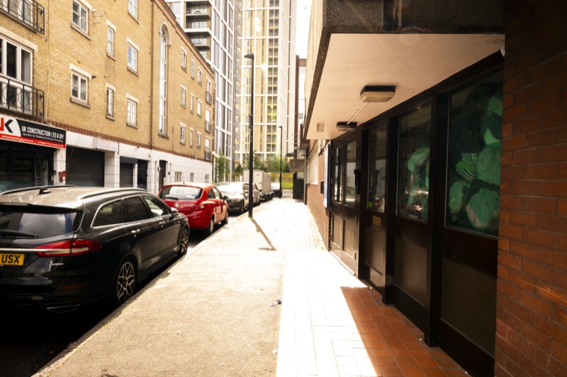 The side street beside 212 in late afternoon light: parked cars, an entrance vestibule visible at right.
